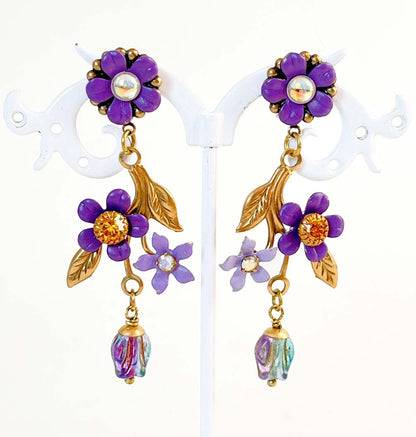 Aros largos Violetas Silvestres con flores violeta, hojas doradas, cristales y cuentas de vidrio de Atelier de Bijoux.