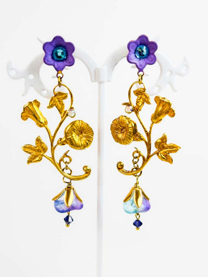 Aros largos dorados de inspiración botánica con ramas, hojas, flores violetas y cristales