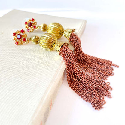 Aros largos vintage con cristales rojos y borlas metálicas doradas estilo barroco.