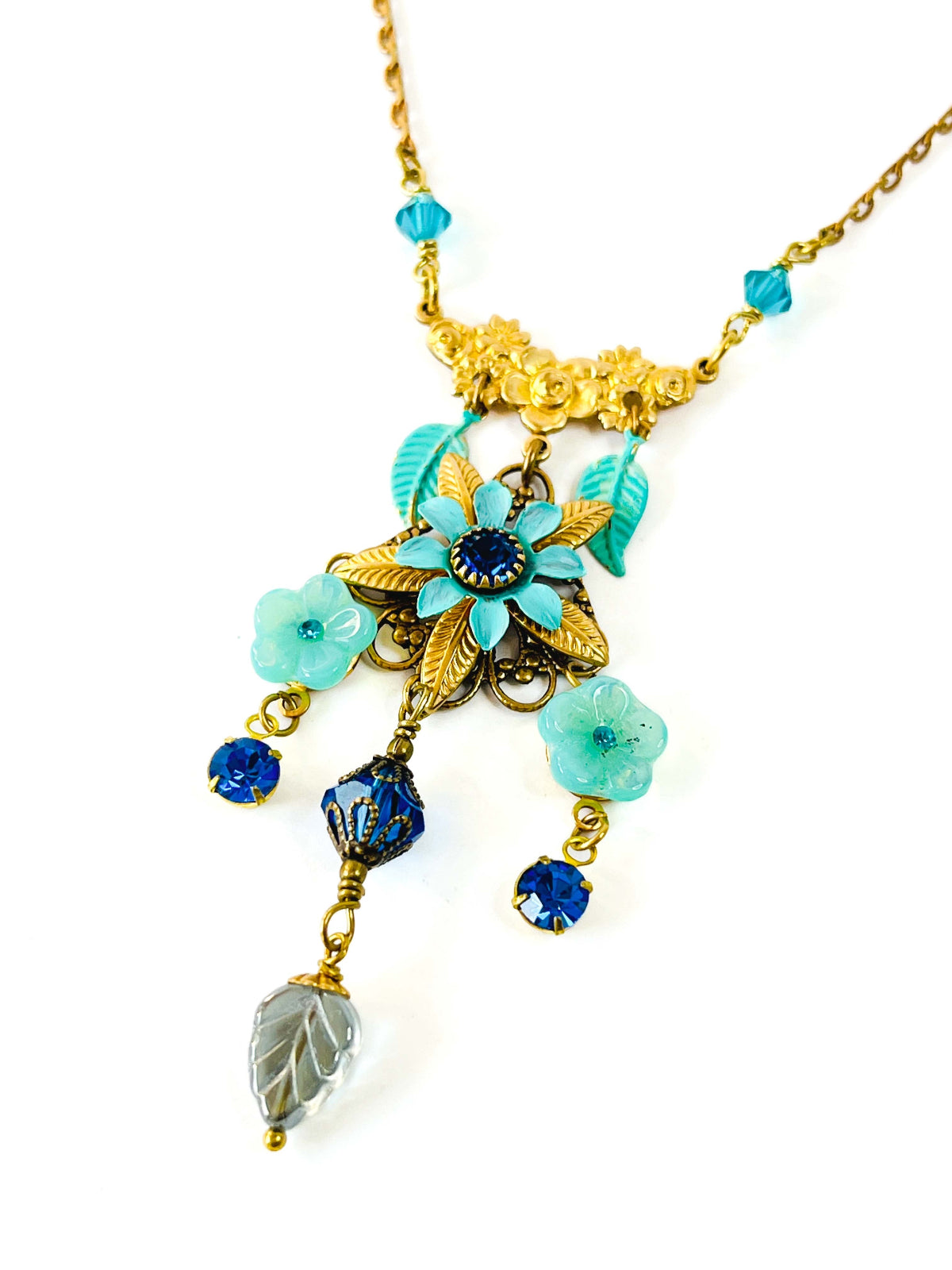 Collar colgante floral, con pieza central de flor triple esmaltada, cristal de swarovski, cuentas y hojas de vidrio checo y metal. En varios tonos de azul.