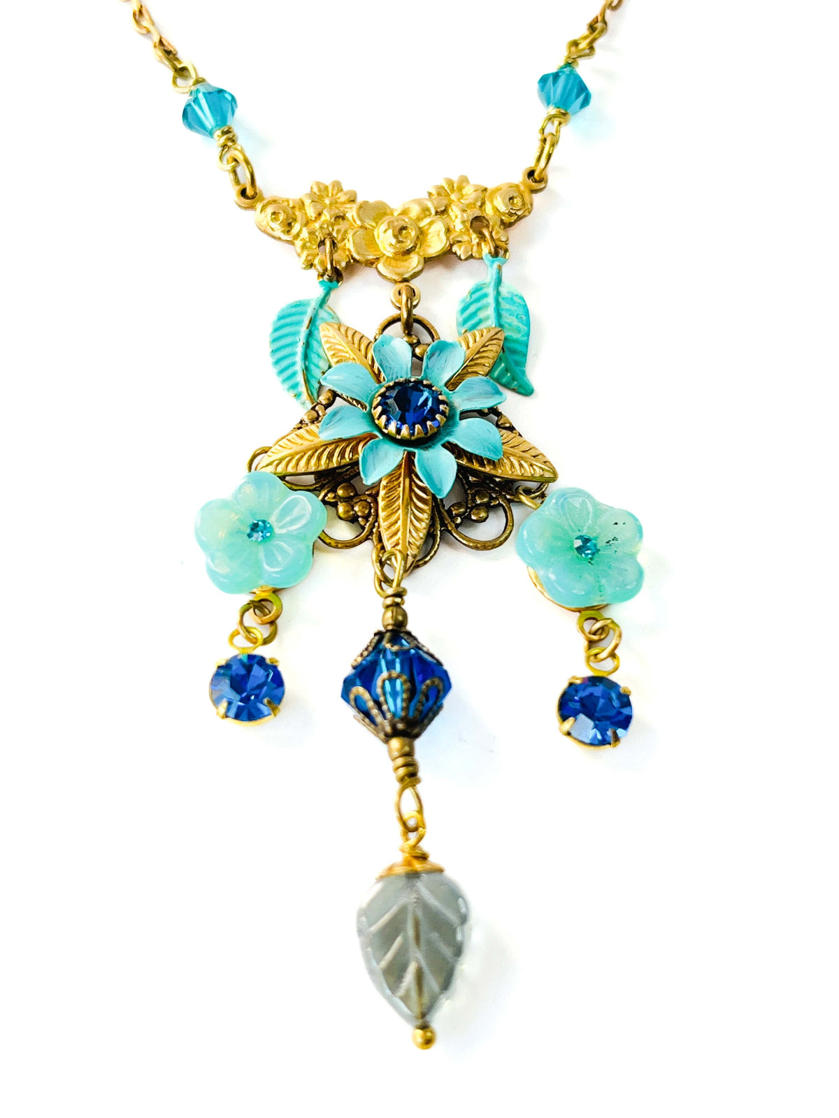 Collar colgante floral, con pieza central de flor triple esmaltada, cristales de Swarovski, cuentas y hojas de vidrio checo y metal. En varios tonos de azul.