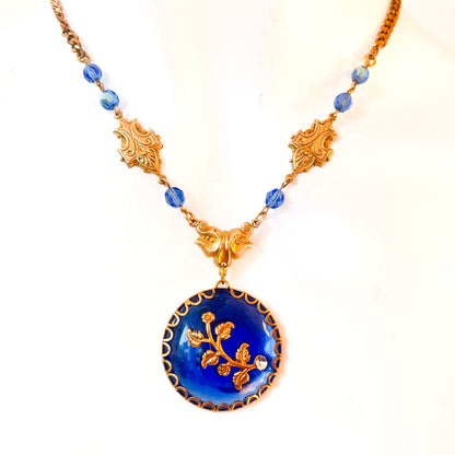 Collar artesanal con medallón azul cobalto, motivos florales dorados y cristales azules de Atelier de Bijoux