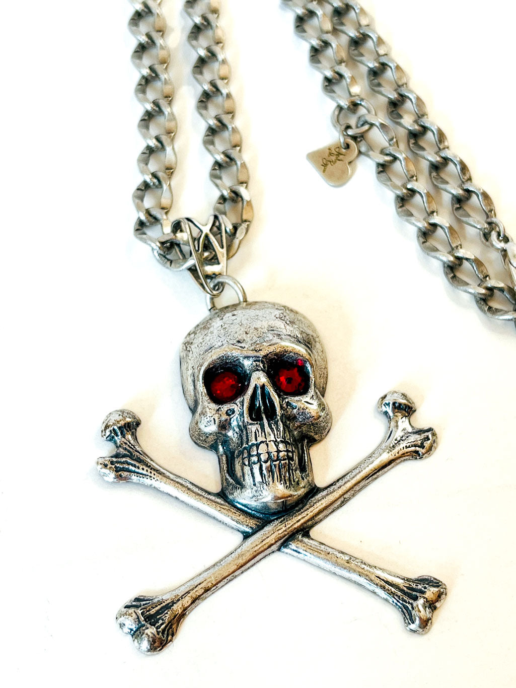 Collar calavera con tibias cruzadas, cristales rojos y cadena en tono plateado envejecido