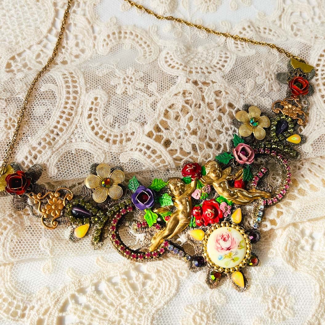 Detalle de collar artesanal con querubines, flores multicolor y cristales sobre encaje