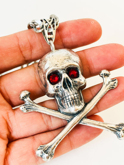 Detalle de gran colgante de calavera con ojos de cristal rojo y tibias cruzadas