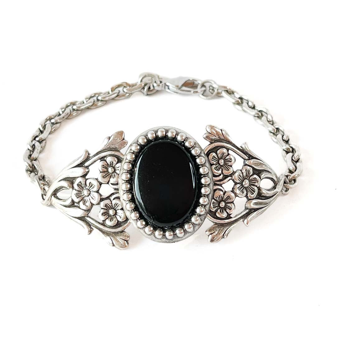 Pulsera victoriana floral en tono plata envejecida con piedra ovalada negra y detalles ornamentales vintage.