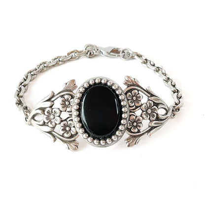 Pulsera victoriana floral en tono plata envejecida con piedra ovalada negra y detalles ornamentales vintage.
