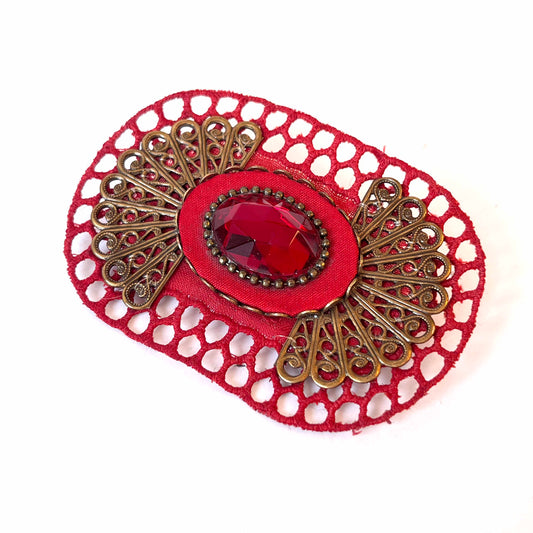 prendedor hecho a mano, con textil bordado y gema roja